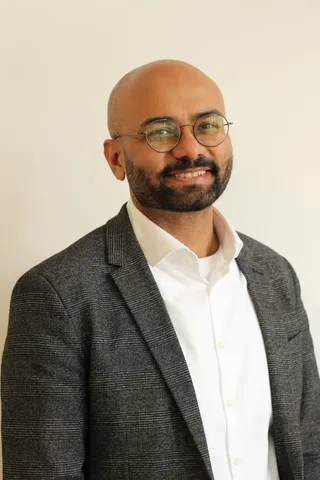 Indrajeet Patil, a man with round gold-framed glasses wearing a dark suit jacket and white shirt